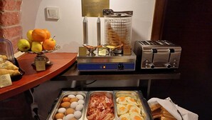 Un bufé de desayuno con alimentos identificados, que incluye frutas, huevos, tocino y pan.