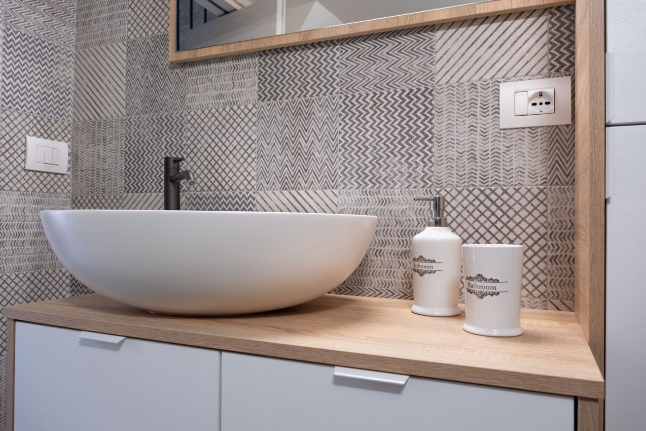 Een badkamer met een grote wastafel, twee witte badkameraccessoires en een spiegel boven de wastafel.