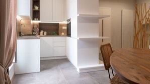 A modern kitchen with white cabinetry, a built-in oven, and a dining area with a wooden table and wicker chairs. - Arco Miraglia suite - Apulia Houses & Flats (Ruvo di Puglia)