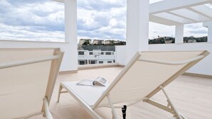 Una terraza abierta con dos sillones blancos, una mesita y vistas a edificios a lo lejos.