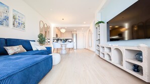 Una sala de estar moderna con un sofá azul, un comedor y una cocina con un televisor grande.