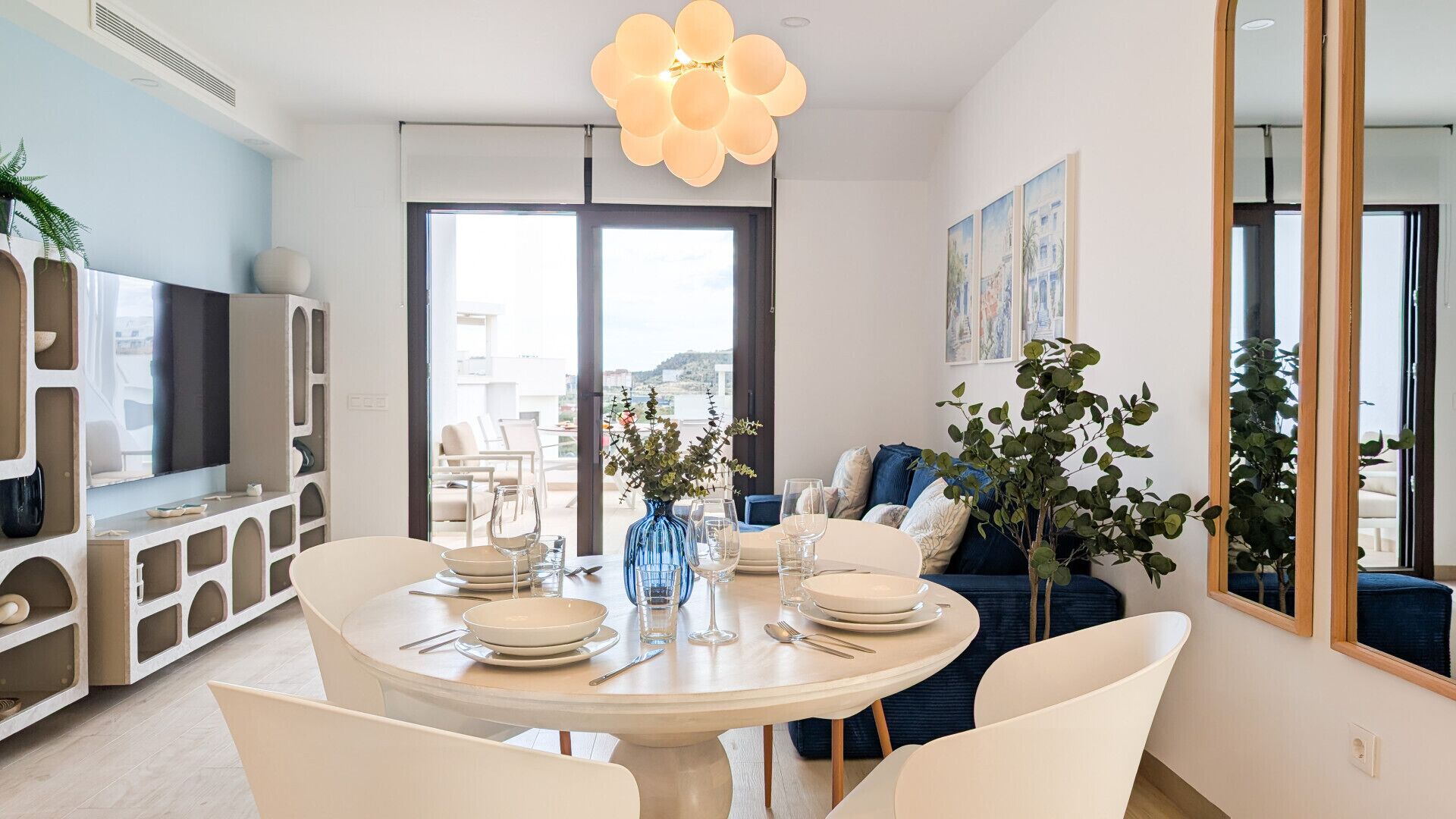 Un espace repas moderne avec une table ronde pour quatre personnes, un téléviseur et une grande fenêtre donnant sur l’extérieur.