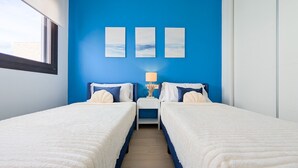 Habitación de hotel con dos camas, una mesita de noche con lámpara y tres cuadros enmarcados en la pared.
