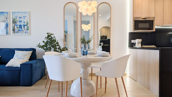 Una cocina moderna con un refrigerador negro, armarios de madera y una zona de comedor con una mesa redonda y sillas blancas.