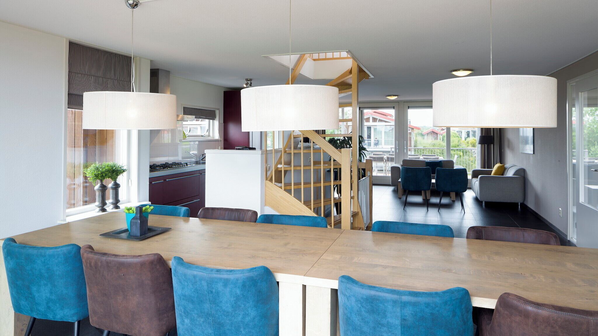 A modern kitchen with a central island, a dining area with blue chairs, and a staircase leading to an upper level.