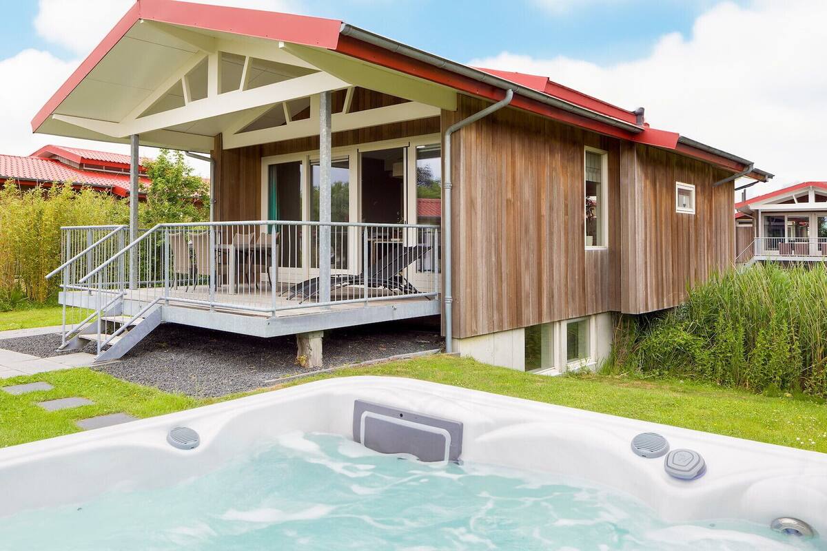 A wooden cabin with a balcony, a hot tub, and a grassy yard.
