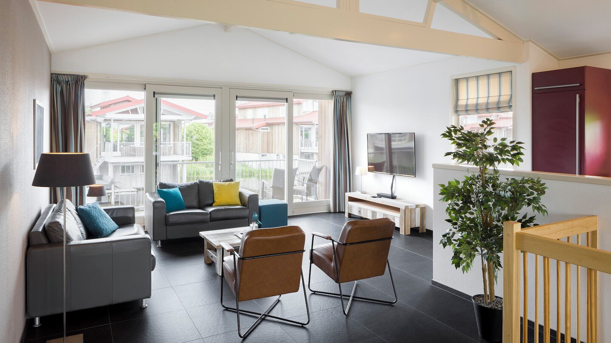A modern living room with a sofa, two armchairs, a coffee table, a TV, and a potted plant.