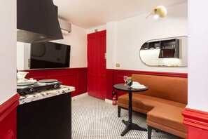 Une cuisine de taille réduite, avec un fourneau, une porte rouge et un miroir qui reflète l’intérieur de la cuisine.