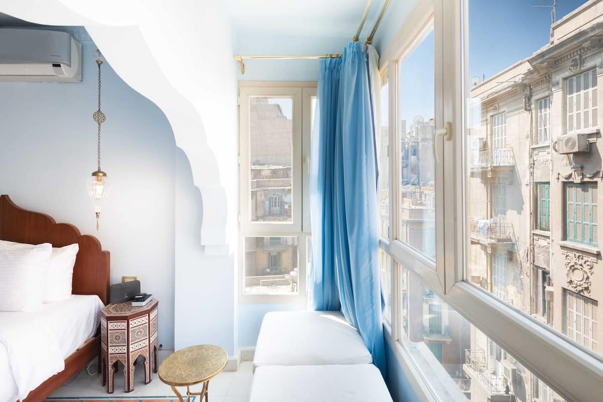 A bedroom with a bed, bedside table, and a window with a view of the city.
