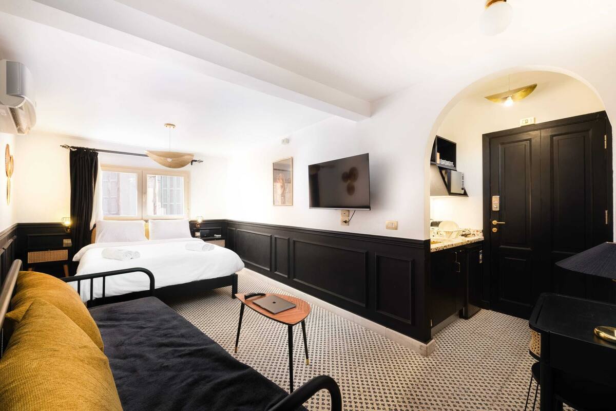 A hotel room with a bed, a desk, a TV, and a kitchenette.