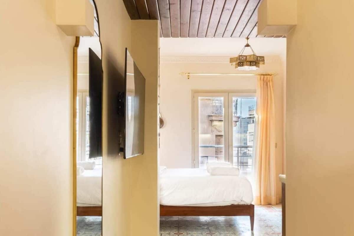 A hallway leading to a bedroom with a patterned floor, a bed, and a window with curtains.