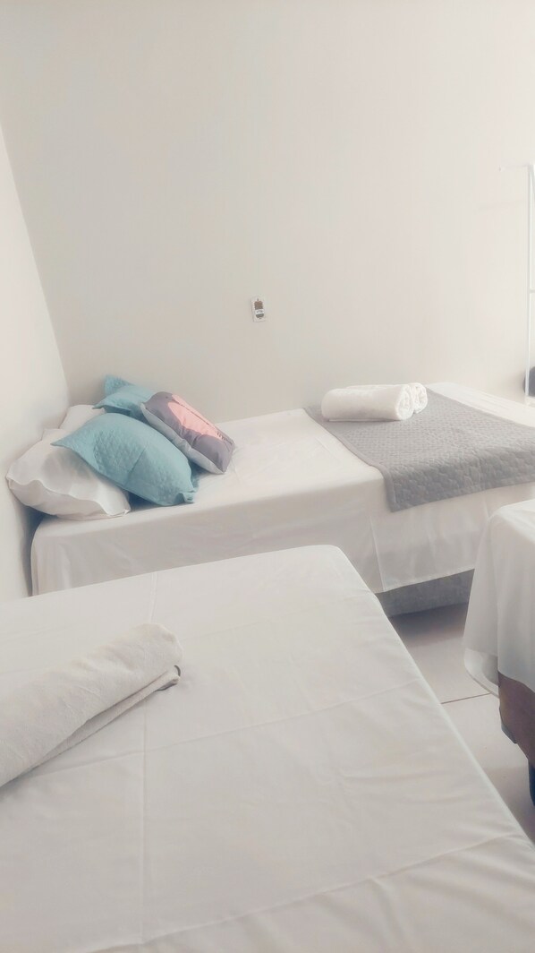 Une chambre simple et épurée, avec deux lits simples, chacun étant équipé de draps et d’oreillers blancs.