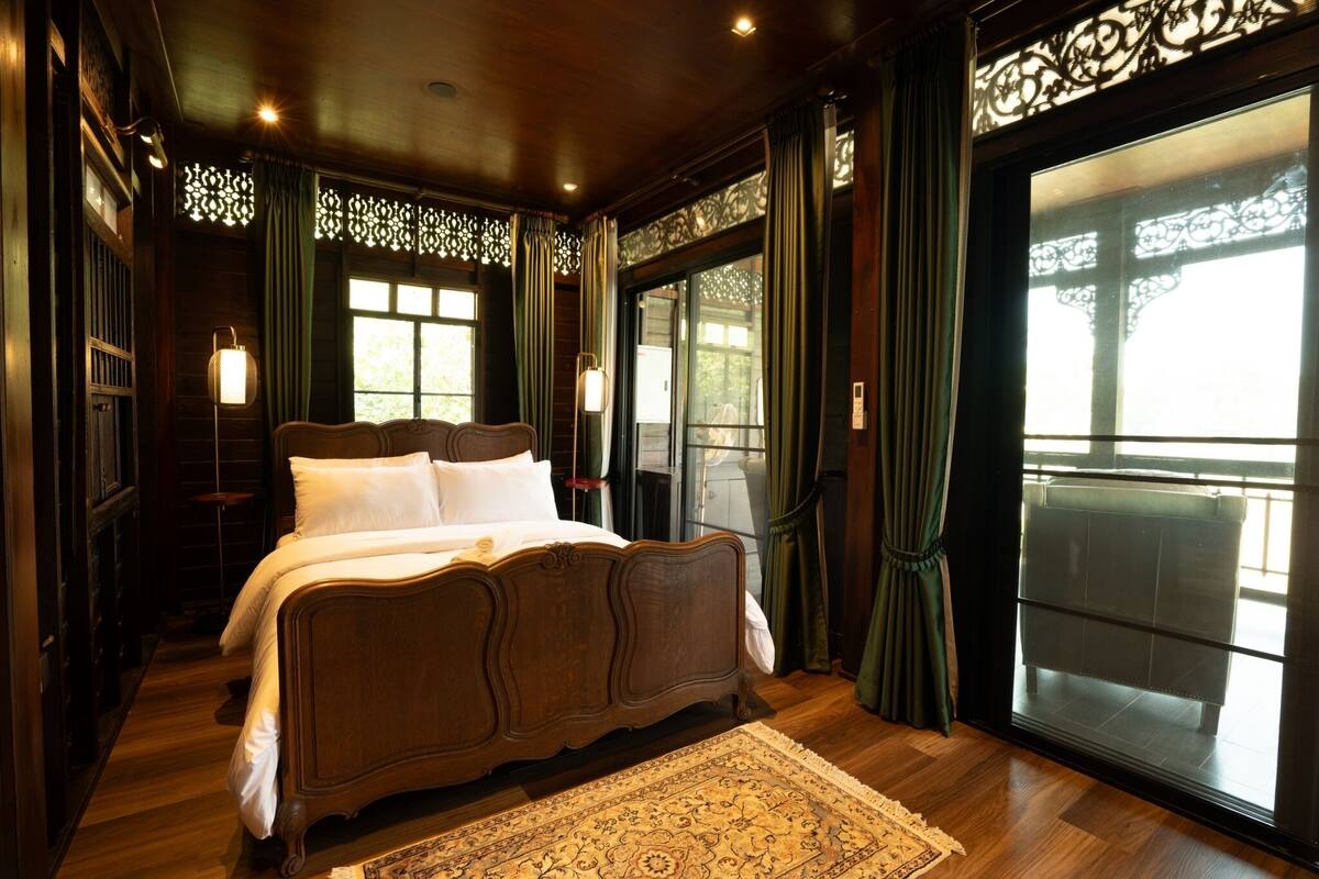 A traditional wooden bed with white linens, a patterned rug, and a large window with curtains.