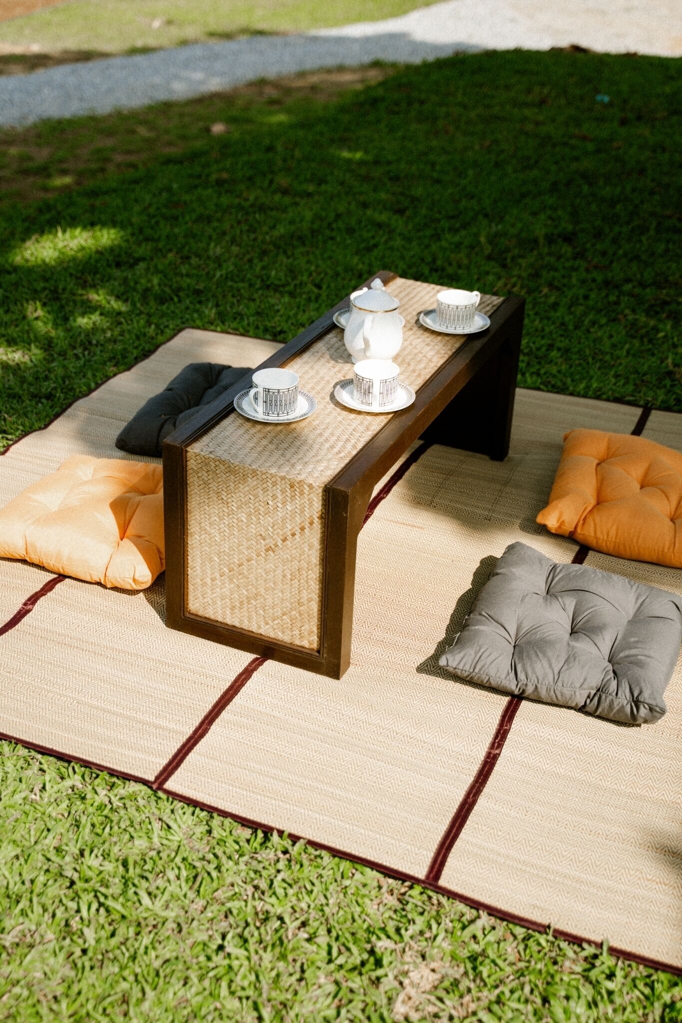 Un montaje para picnic con una mesa, cojines y una tetera sobre una zona cubierta de césped.
