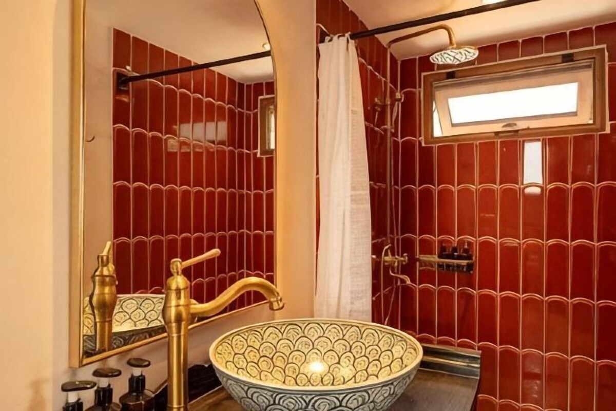 A bathroom with a large bowl sink, a shower, a window, and a mirror.