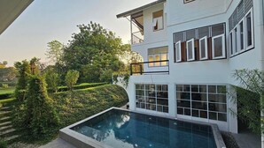 A modern two-story house with a swimming pool, surrounded by lush greenery and trees. - Akara House Sukhothai (Si Satchanalai)