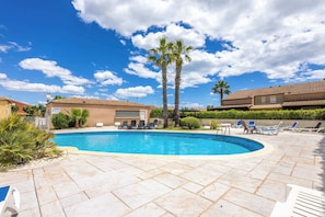 Ein Pool mit Liegestühlen, Palmen und blauem Himmel.