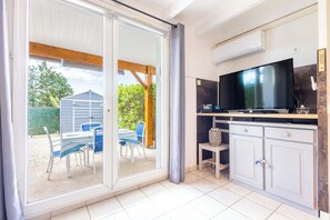 A room with a sliding glass door leading to an outdoor patio, a flat-screen TV, a small cabinet, and a tiled floor.