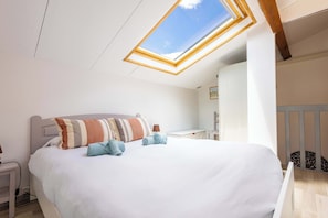 Ein Schlafzimmer mit Dachfenster, einem Bett mit Kissen, einem Nachttisch und einem Babybett.