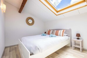 Une chambre avec un puits de lumière, un lit avec une literie blanche, une table de chevet avec une lampe et une horloge murale.