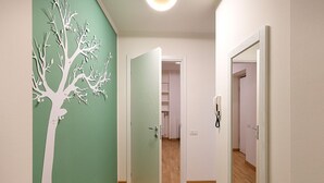 A hallway with a green wall and a white tree decoration, leading to a room with a door and a phone on the wall. - easyhomes - Repubblica (Milan)