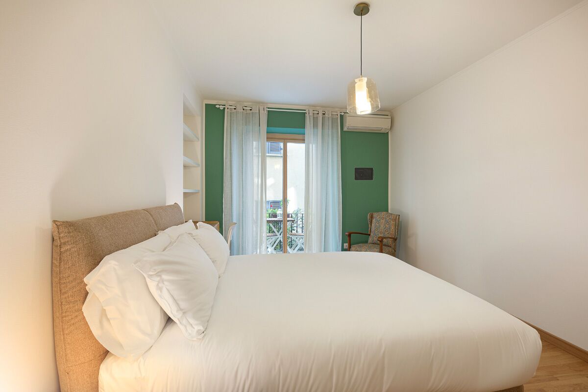 A bedroom with a bed, a chair, a window with curtains, and an air conditioning unit.