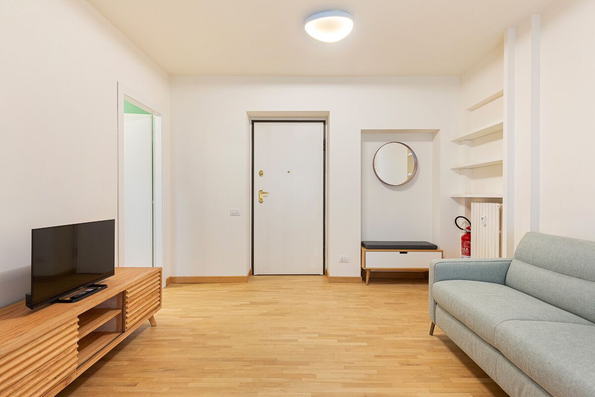 A modern living room with a wooden entertainment unit, a light blue sofa, and a white door with a circular mirror above it.