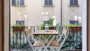 A wooden table with chairs on a balcony with a view of a building with shutters. - easyhomes - Repubblica (Milan)