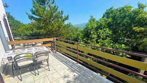 Une terrasse avec une table et des chaises, une balustrade en bois et une vue sur les arbres et les collines.