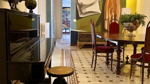 A dining area with a piano, a table with chairs, a vase with a plant, and a large painting on the wall. - The House of Paintings Spacious cozy art house in the heart of the Palermo city (Palermo)