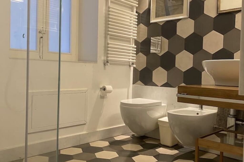 A bathroom with a hexagonal tile floor, a toilet, a bidet, and a glass shower enclosure.