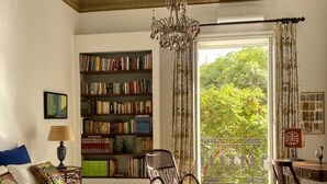 A room with a large bookshelf, a bed, a chair, and a balcony with curtains. - The House of Paintings Spacious cozy art house in the heart of the Palermo city (Palermo)