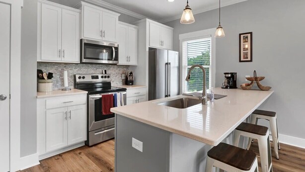 A modern kitchen with white cabinets, stainless steel appliances, a large island with stools, and pendant lighting. - The Beacon, Steps From The Beach (Carolina Beach)