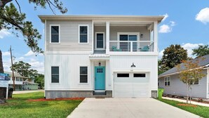 A two-story house with a front garage, a balcony on the upper floor, and a green door. - The Beacon, Steps From The Beach (Carolina Beach)