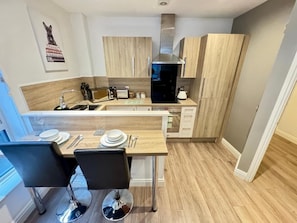 Een moderne keuken met houten kastjes, een ingebouwde oven en een eethoek met twee stoelen en een tafel gedekt voor twee personen.