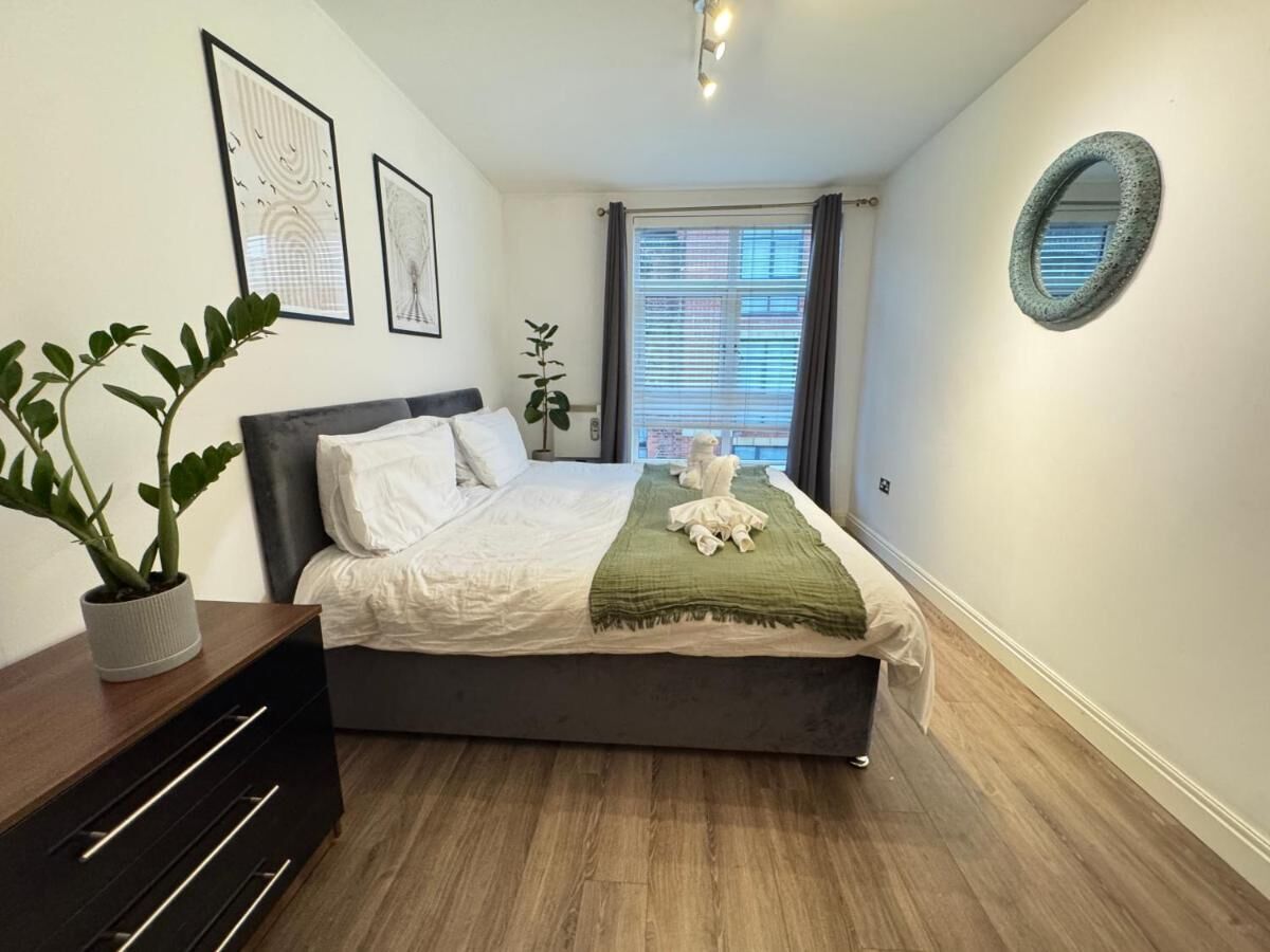 A bedroom with a bed, a bedside table, a potted plant, and a window with curtains.