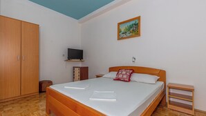 A bedroom with a wooden bed, a television on a shelf, a painting on the wall, and a wardrobe. - Apartman Franjo 1 (Dramalj)