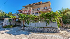 A multi-story residential building with balconies, a stone wall, and a garden with vines. - Apartman Franjo 1 (Dramalj)