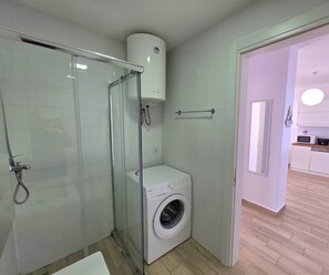 Enjoy a convenient and modern bathroom with a glass-enclosed shower and washing machine.