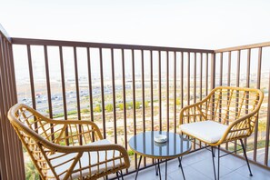Een balkon met twee rieten stoelen en een klein, rond tafeltje, met uitzicht op een stadsgezicht met wegen en gebouwen.