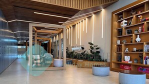 Un moderno vestíbulo de hotel con un mostrador de recepción de madera, una zona de estar y una estantería llena de libros y objetos decorativos.
