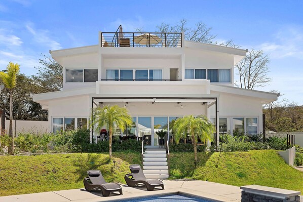 Une maison moderne à deux étages, dotée d’une piscine, d’un espace salon extérieur et d’un escalier menant à l’entrée.