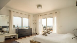 A modern bedroom with a large bed, a vanity, and a view of the city. - Spacious 3BR Villa with pool and views (Fuengirola)