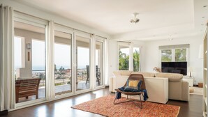 A spacious living room with a large sliding glass door leading to an outdoor patio, a comfortable seating area with a sofa and a chair, and a flat-screen TV on a stand. - Spacious 3BR Villa with pool and views (Fuengirola)