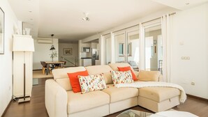 A modern living room with a beige sectional sofa, a glass coffee table, and a dining area in the background. - Spacious 3BR Villa with pool and views (Fuengirola)