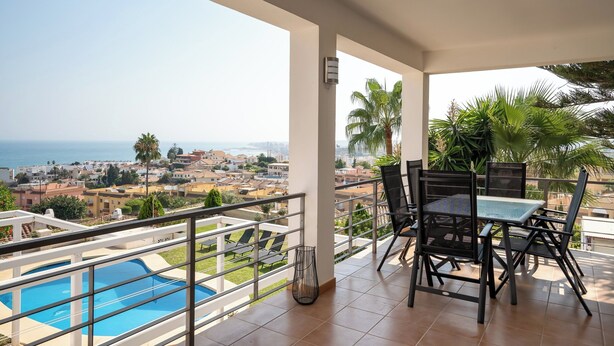 A balcony with a pool, outdoor seating, and a view of the sea and town. - Spacious 3BR Villa with pool and views (Fuengirola)