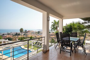 A balcony with a pool, outdoor seating, and a view of the sea and town. - Spacious 3BR Villa with pool and views (Fuengirola)