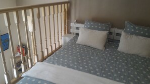 Un dormitorio con cama, almohadas, una mesita de noche y una barandilla de madera.