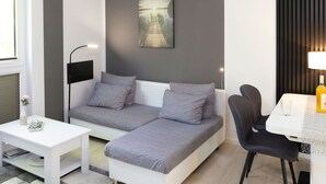 A modern, compact living space with a sofa, a small table, a chair, and a dining area.
