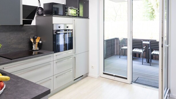 A modern kitchen with a built-in oven, microwave, and a small refrigerator. There is a sliding glass door leading to an outdoor patio with a table and chairs.